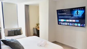 Une chambre d’hôtel dotée d’un grand téléviseur à écran plat fixé au mur, diffusant une chaîne d’information, d’un lit bien fait avec des oreillers, d’un bureau avec une chaise et d’une fenêtre avec des rideaux.