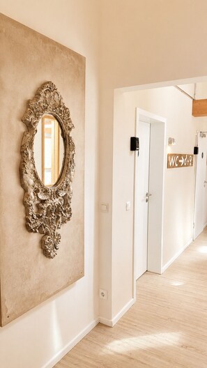 Un pasillo con un espejo grande y ornamentado, una puerta blanca con el cartel 'WC' y suelo de madera.