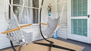 Twee hangmatten aan een veranda, met een witte deur en ramen op de achtergrond.