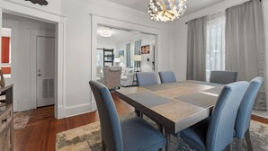 Een eethoek met een houten tafel, blauwe fauteuils en een moderne kroonluchter.