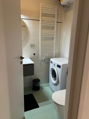 A compact bathroom with a washing machine, a toilet, a sink, and a towel rack. - Two-room apartment 2 min from Bocconi University and 10 from the subway (Milano)