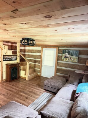 L’intérieur d’une cabane en rondins, avec une cheminée, un escalier, un canapé et une porte.