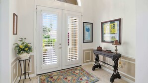 A hallway with a white door, a potted plant, a table with a lamp, and a framed picture on the wall. - Relax All Season: Pool, Spa & Golf Included (Bonita Springs)