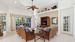 A spacious living room with a high ceiling, a ceiling fan, a fireplace, and a television. - Relax All Season: Pool, Spa & Golf Included (Bonita Springs)
