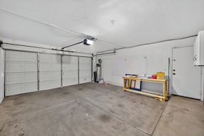 Un garage avec trois portes doubles, un établi équipé d’outils et un panneau perforé fixé au mur.