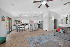 A spacious living area with a kitchen, dining area, and a ceiling fan.