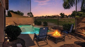 A backyard with a swimming pool, a fire pit, and outdoor seating.