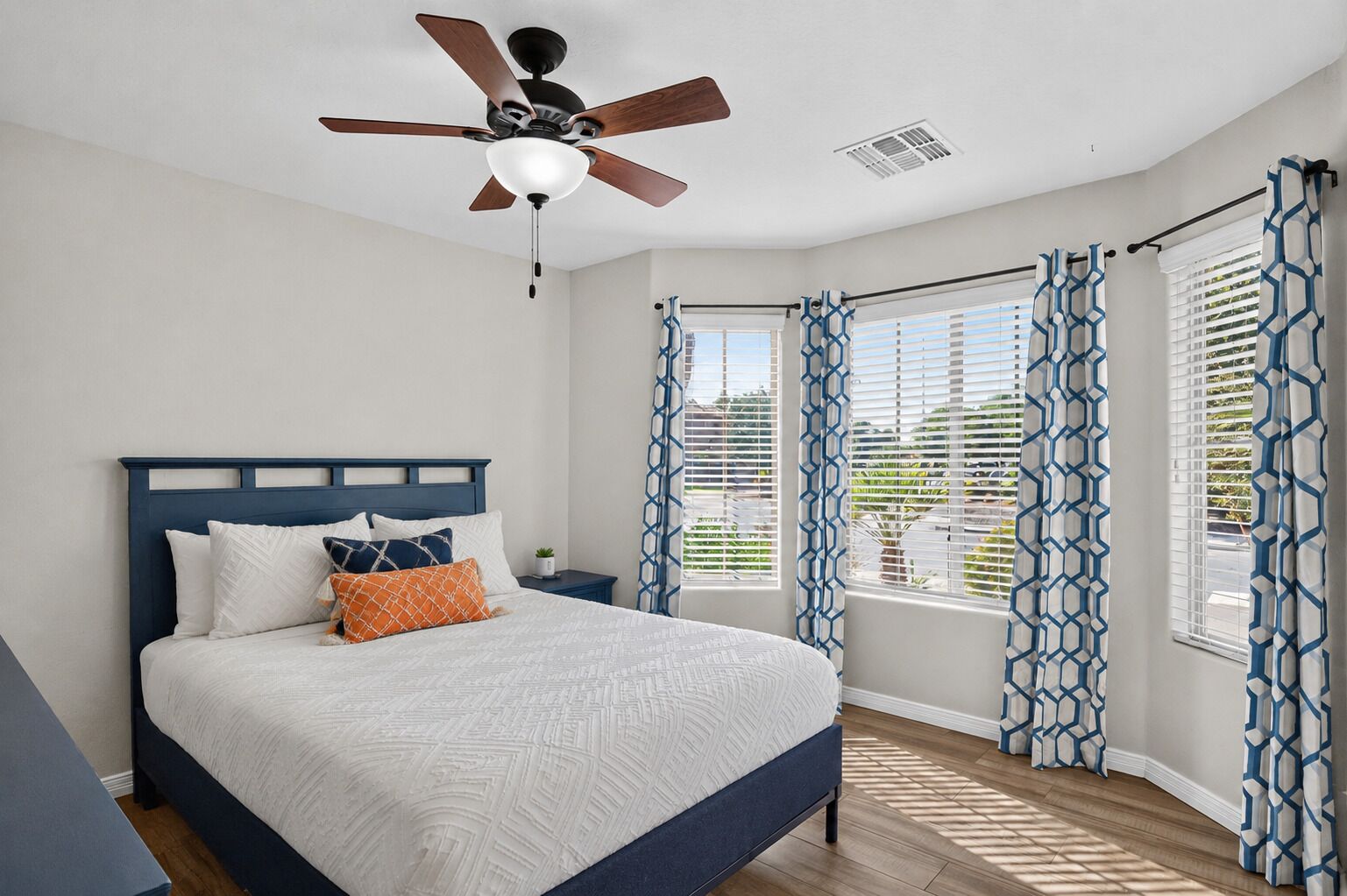 A bedroom with a bed, a nightstand, a ceiling fan, and patterned curtains.