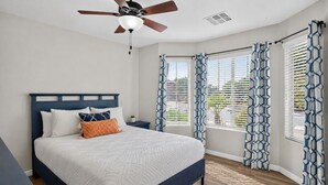A bedroom with a bed, a nightstand, a ceiling fan, and patterned curtains.