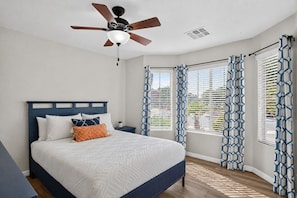 A bedroom with a bed, a nightstand, a ceiling fan, and patterned curtains.