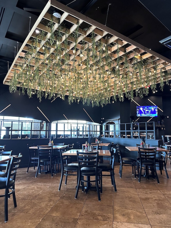 A restaurant interior with a modern design, featuring hanging plants and a bar area.