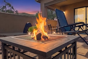 An outdoor patio with a fire feature, seating, and a view of the sky.