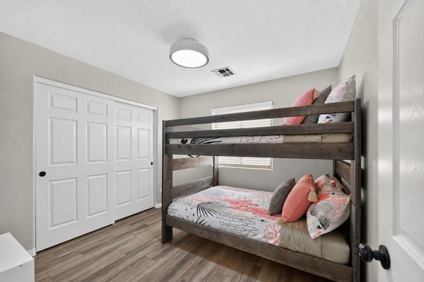 Un lit superposé avec une couvre-lit et des oreillers à motifs, une porte blanche et un luminaire au plafond.