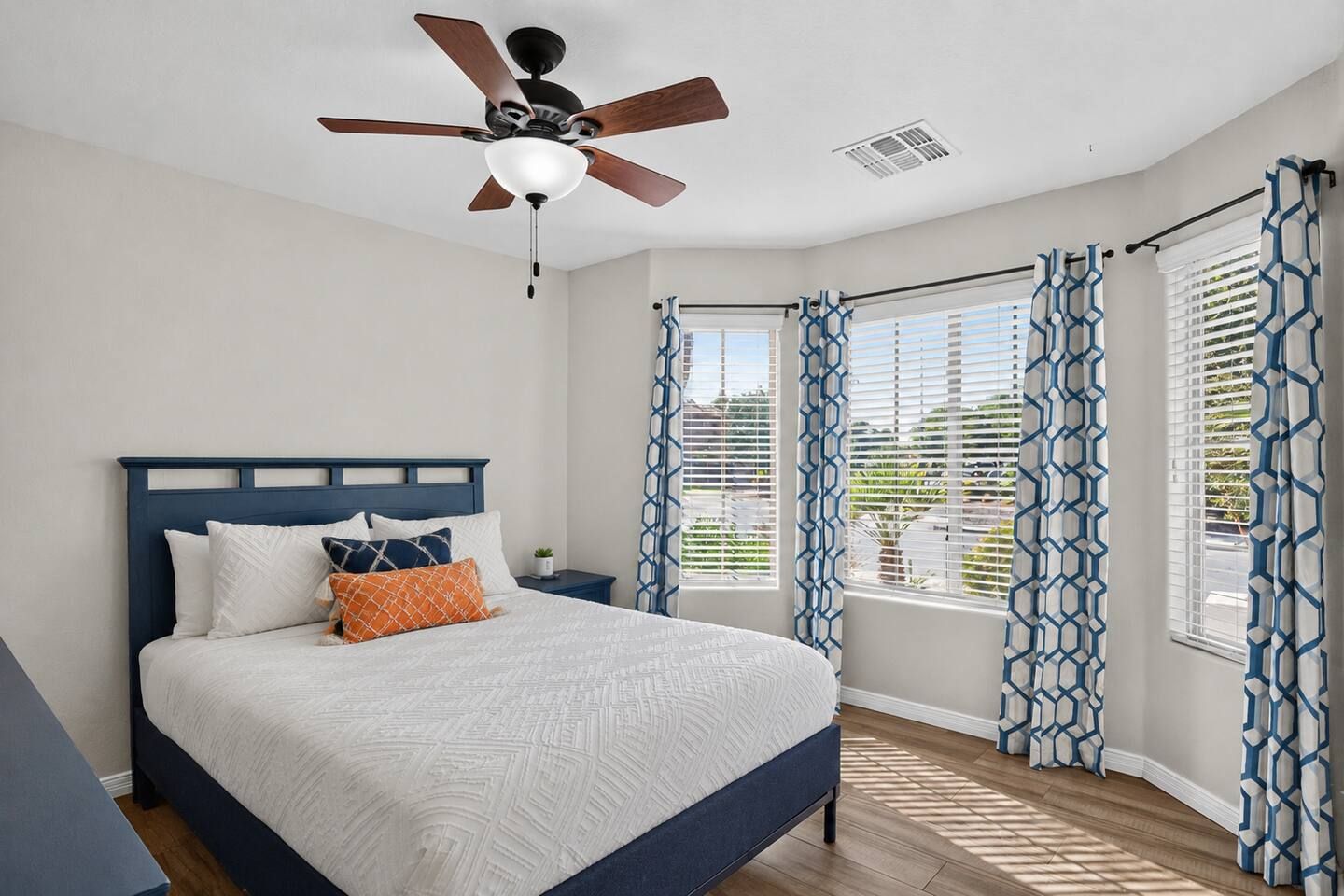 Une chambre à coucher avec un lit, une table de chevet, un ventilateur de plafond et des rideaux à motifs.