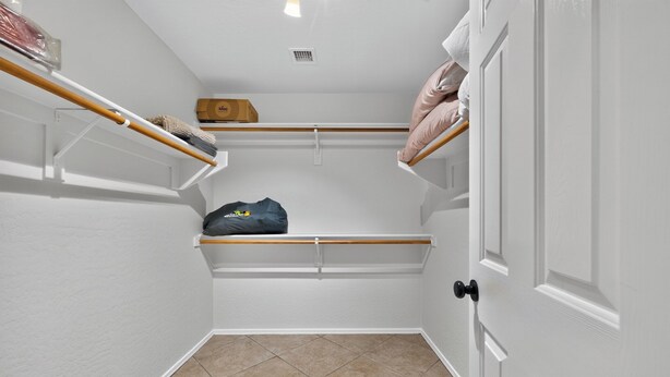 A small, enclosed closet with white walls, a tiled floor, and a door with a black handle.