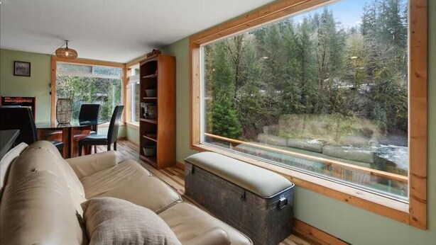 A cozy living room with a large window overlooking a forested area and a river. - The Salmon Hole (Washougal)
