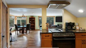 A kitchen with a central island, wooden cabinets, a stove, and a dining area with chairs and a table. - The Salmon Hole (Washougal)