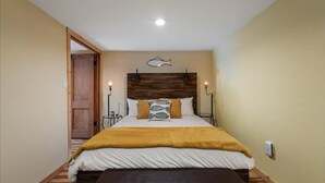 A bedroom with a wooden headboard, a bed with a white and yellow bedspread, two bedside lamps, and a small fish wall decoration. - The Salmon Hole (Washougal)