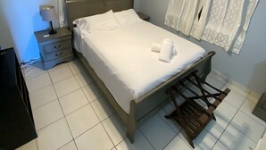 Una cama bien tendida con sábanas blancas, un ventilador de techo y una mesita de noche con lámpara.