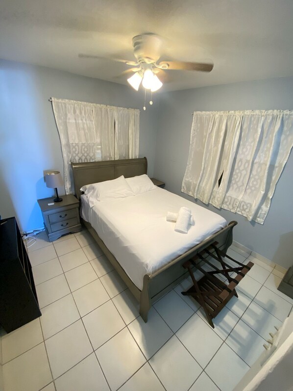 A neatly made bed with white linens, a ceiling fan, and a bedside table with a lamp. - Seabreeze Family Beach Retreat/Private Hot Tub near Amazing Beaches (Arecibo)