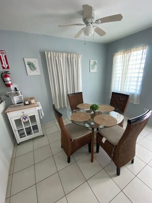 A dining area with a round glass table, wicker chairs, and a ceiling fan. - Seabreeze Family Beach Retreat/Private Hot Tub near Amazing Beaches (Arecibo)