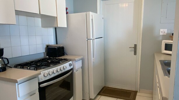 Una cocina compacta con armarios blancos, estufa, horno y refrigerador.