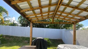 Un espacio al aire libre cubierto con una mesa de madera y bancos, una parrilla y un colchón.