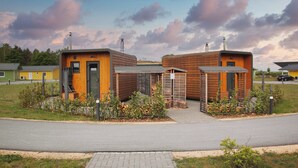 A modern building with a wooden facade, a central entrance, and a small garden area. - Tiny House (Pod) Ole #15 at Bärwalder See - SKAN-PARK (Klitten)