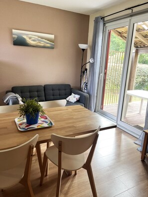 Un coin repas avec une table en bois, des chaises, une plante en pot, un canapé et une vue à travers une porte vitrée.