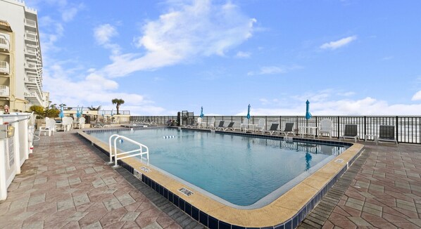 A rooftop swimming pool with a clear view of the ocean, surrounded by lounge chairs and umbrellas.