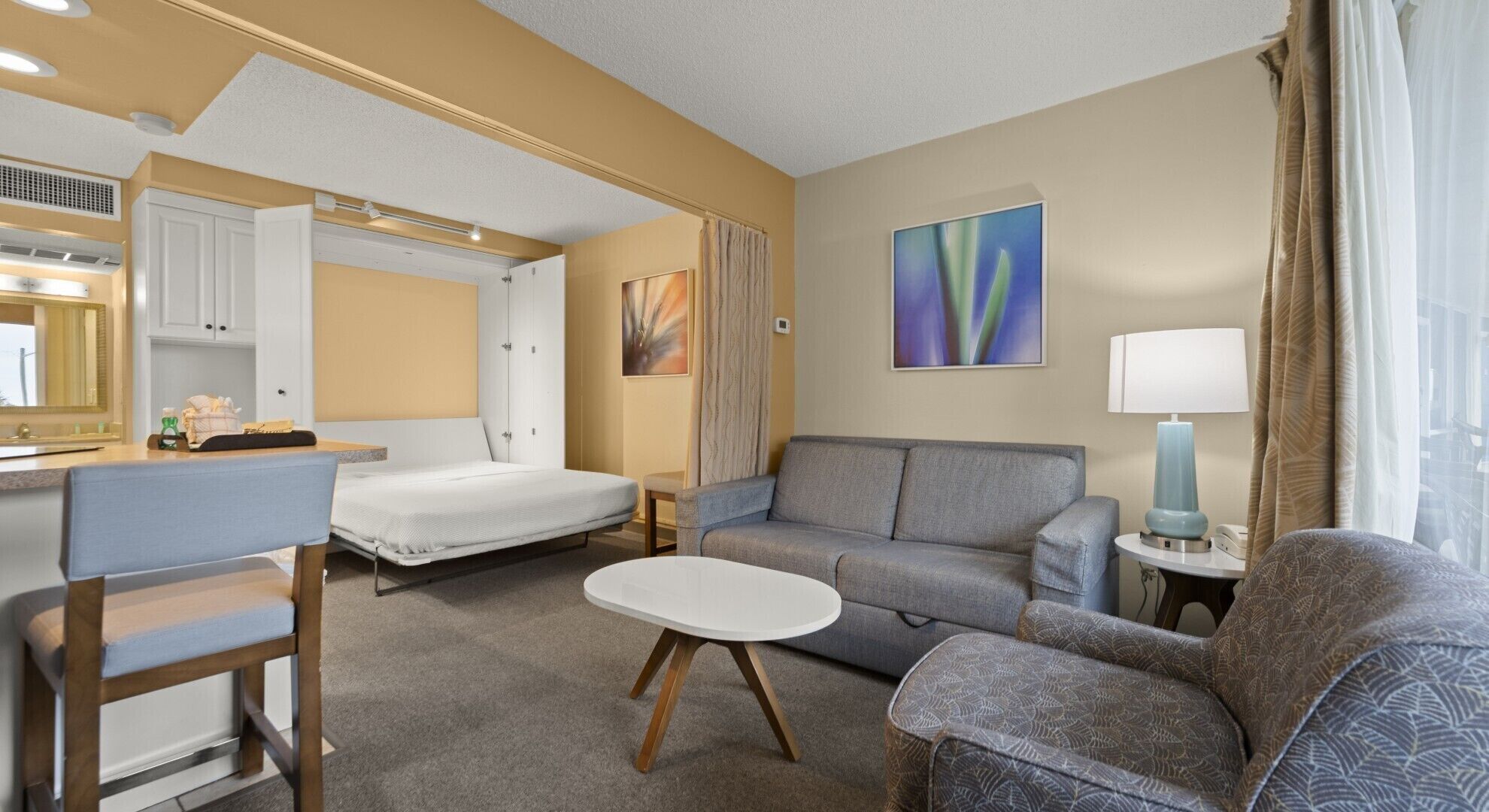 Habitació d'hotel senzilla amb llit, sofà, taula petita, cadira, escriptori i bany amb mirall.