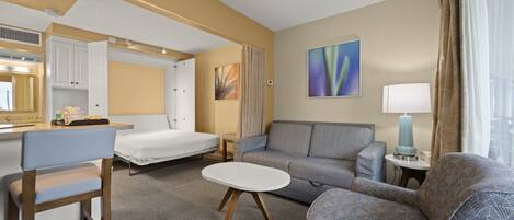Habitació d'hotel senzilla amb llit, sofà, taula petita, cadira, escriptori i bany amb mirall.