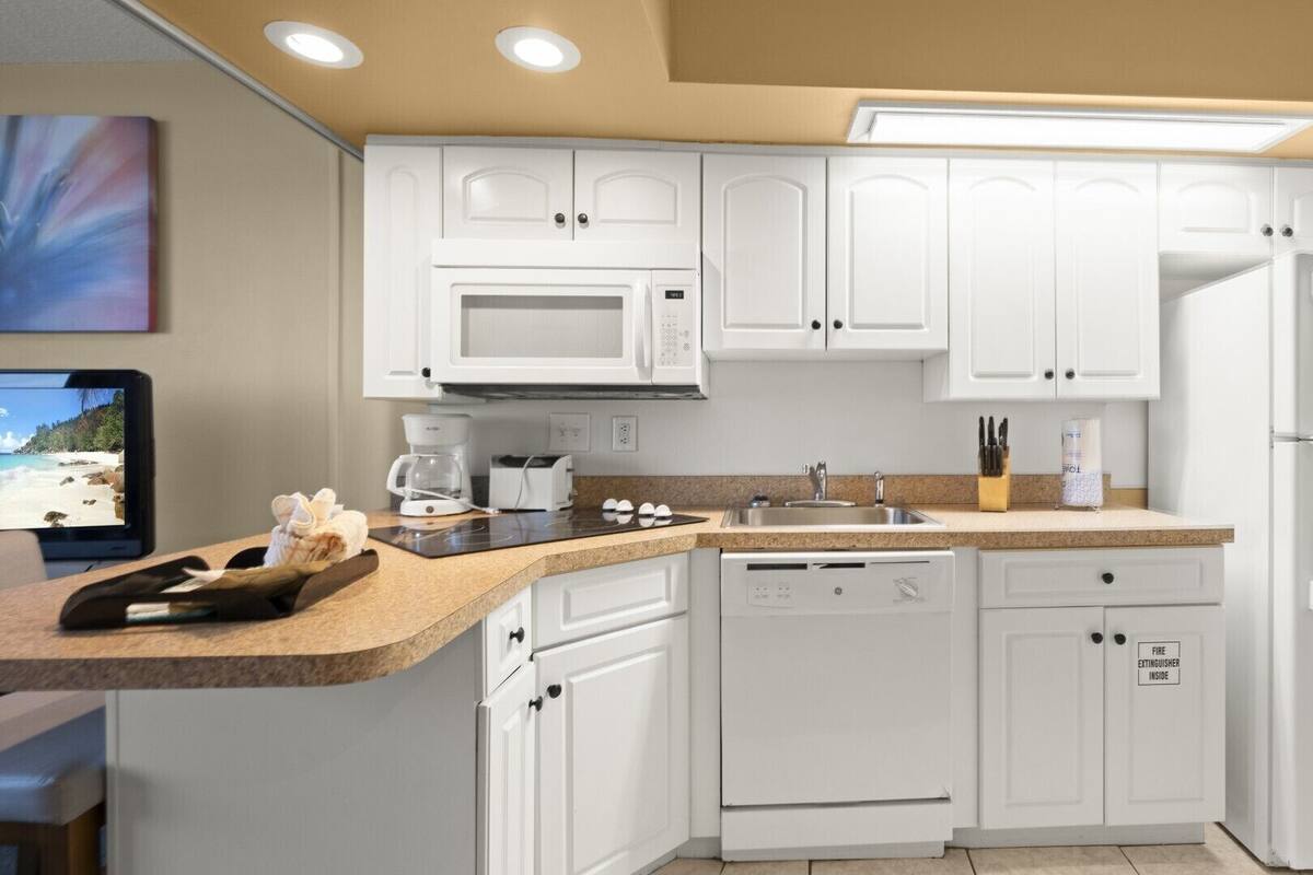 A modern kitchen with white cabinets, a built-in microwave, a coffee maker, and a dishwasher.
