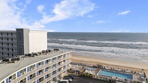 Un hotel frente a la playa con piscina, varios balcones y vista al océano.