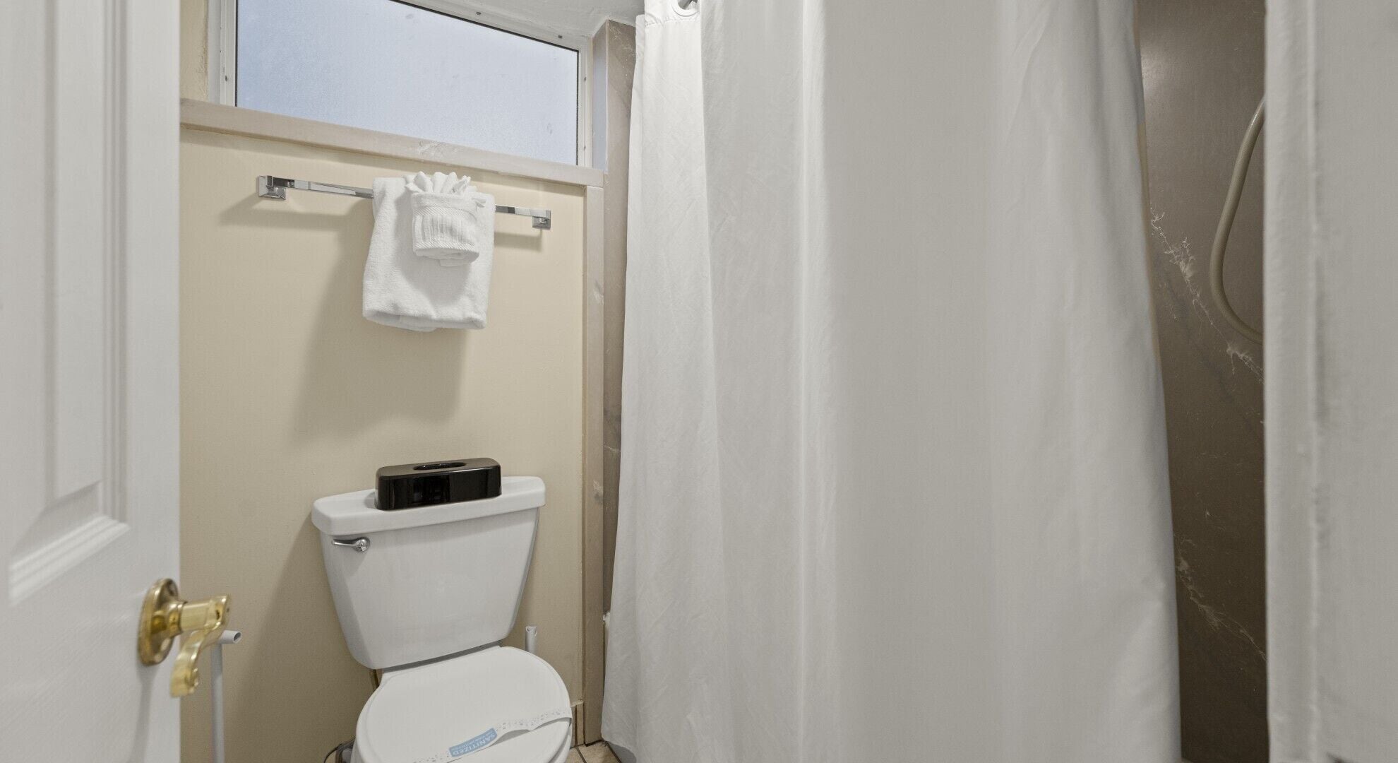 A bathroom with a toilet, a towel hanging on a rack, and a shower curtain.