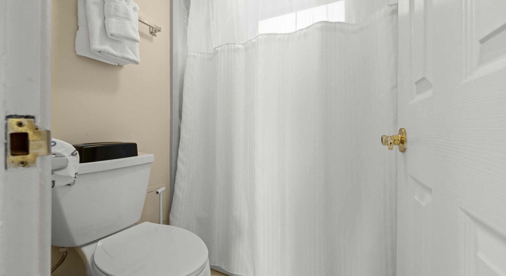 A bathroom with a white toilet, a towel rack, and a shower curtain.