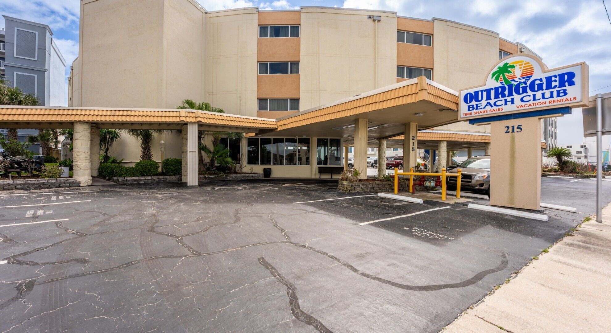 A hotel with a covered entrance, a sign for the Outrigger Beach Club, and a parking lot.