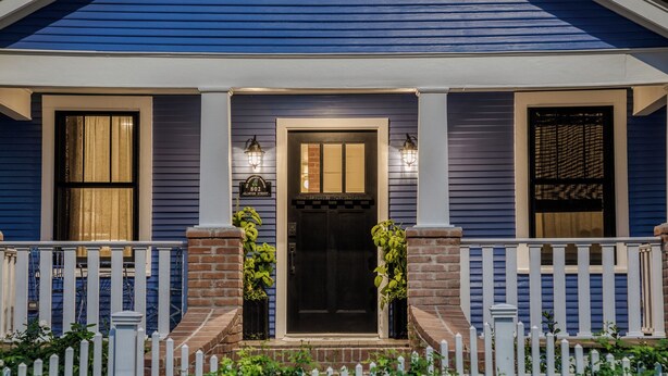 Una casa con una porta d'ingresso scura, due finestre con persiane e un piccolo portico con una recinzione in legno bianco.