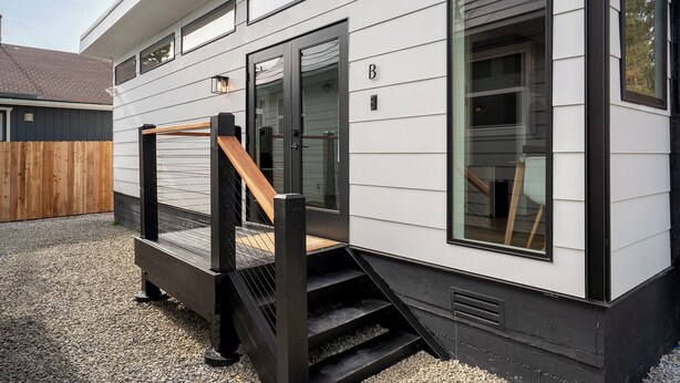 Ein modernes Haus mit einer Holzterrasse, einer schwarzen Treppe und einem großen Fenster.