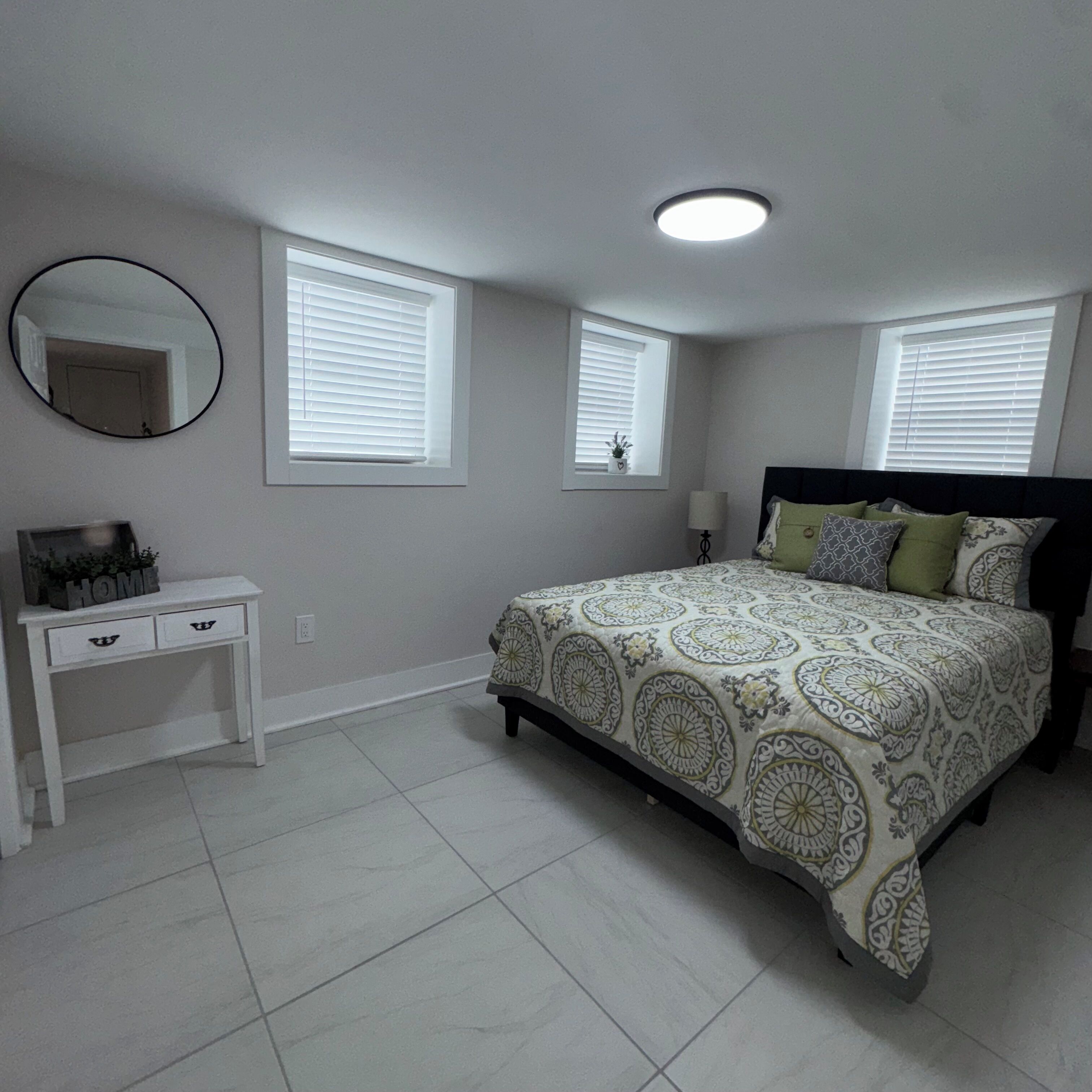 Un dormitorio con cama, mesita de noche, espejo y dos ventanas con persianas.