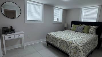 Un dormitorio con cama, mesita de noche, espejo y dos ventanas con persianas.