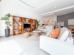 A modern living room with a sofa, TV, wooden shelving unit, and a dining area with a table and chairs. - Villa Hamal by DVH Luxe Retreats 2BR Private Pool Villa Near Canggu (Kabupaten Badung)