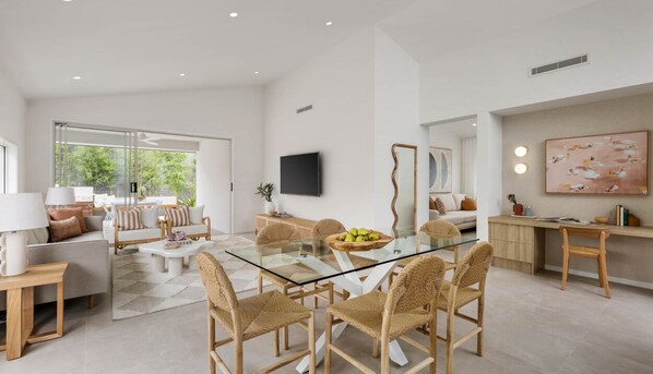 A modern living room with a glass dining table, wicker chairs, and a sofa. There is a TV mounted on the wall and a painting above the sofa. - Modern 2BR Apartment in Ulbroka (Ulbroka)