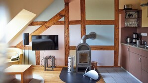 A cozy room with a fireplace, wooden beams, a television, and a kitchen area with cabinets and appliances. - Studio 6 - Träumerei - Quiet studio in the count's forester's lodge (Temmen-Ringenwalde)