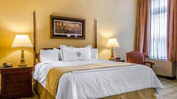 A hotel room with a bed, two bedside tables, a chair, a window with curtains, and a painting on the wall.