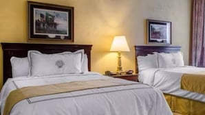 Une chambre d’hôtel avec deux lits, une table de chevet avec une lampe et des tableaux encadrés au mur.