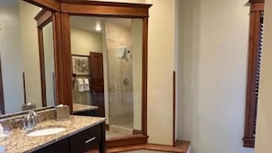 Une salle de bain dotée d’un grand miroir, d’un plan de travail en granit, d’un lavabo et d’un espace douche.