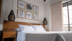 Una cama bien hecha con sábanas blancas, un cabecero de madera y una mesita de noche con una lámpara.