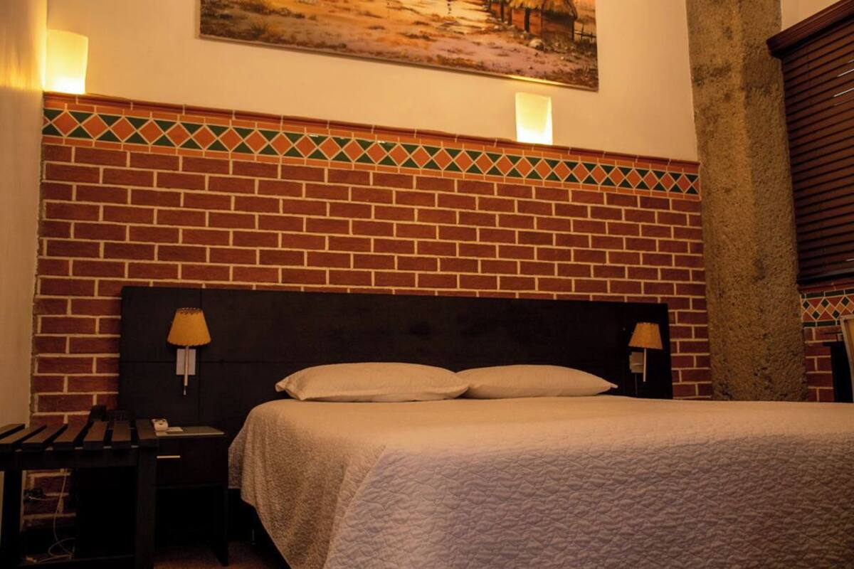 A hotel room with a brick-patterned headboard, a bed with white bedding, two bedside lamps, and a painting on the wall.