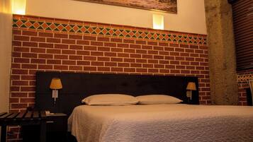 Habitación de hotel con cabecera de ladrillo, cama con ropa de cama blanca, dos lámparas de noche y un cuadro en la pared.